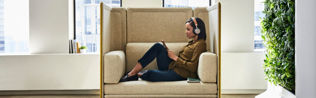 Modern employee wearing headphones on her phone sitting in ergonomic friendly soft office chair