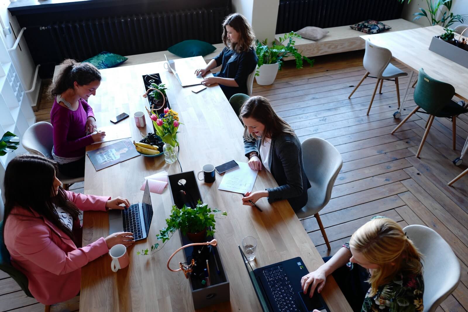 A group of employees working on laptops around a wooden bench desk