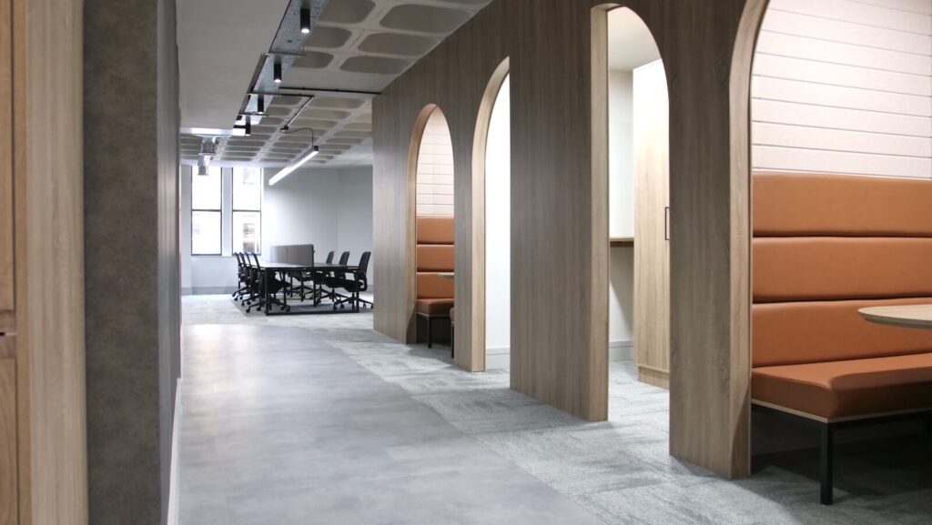Modern office with grey flooring, arched booths with brown leather banquet seating with wooden tables