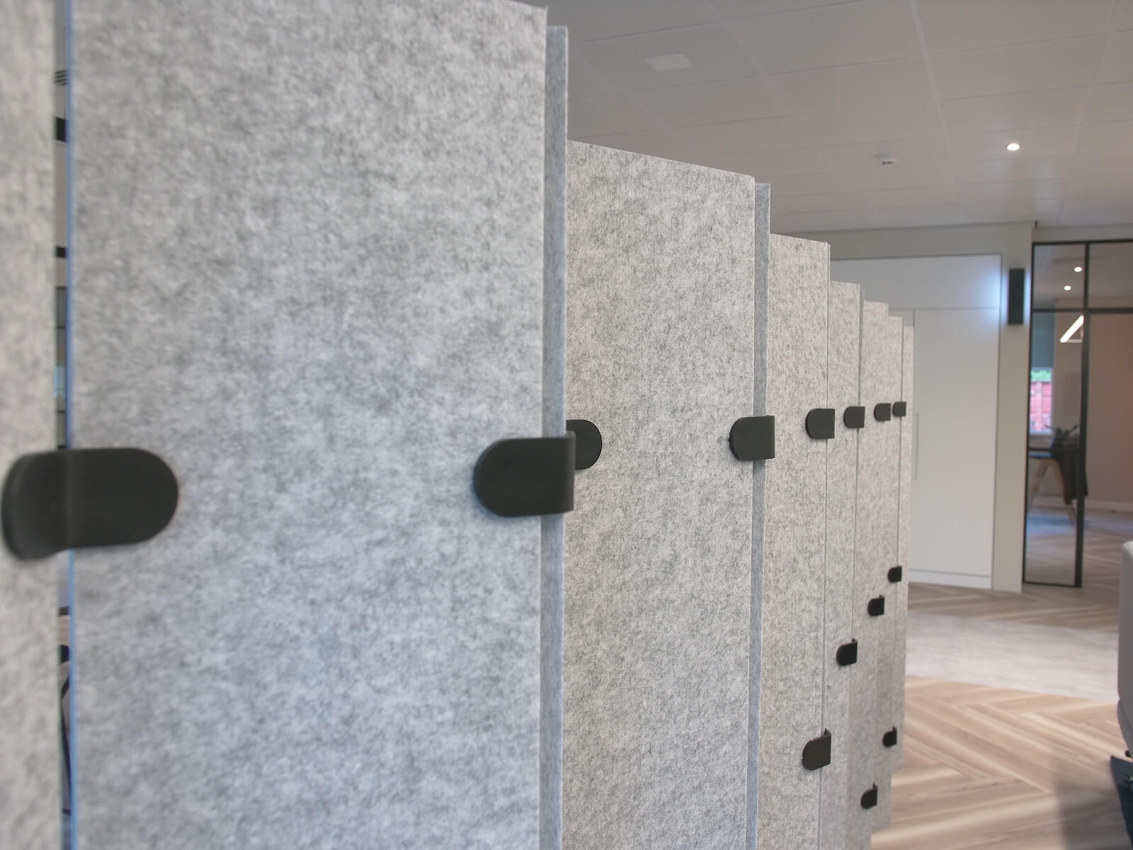 Close up of a grey felt acoustic diving wall in a modern office with spotlights, glass door and grey wood-style flooring