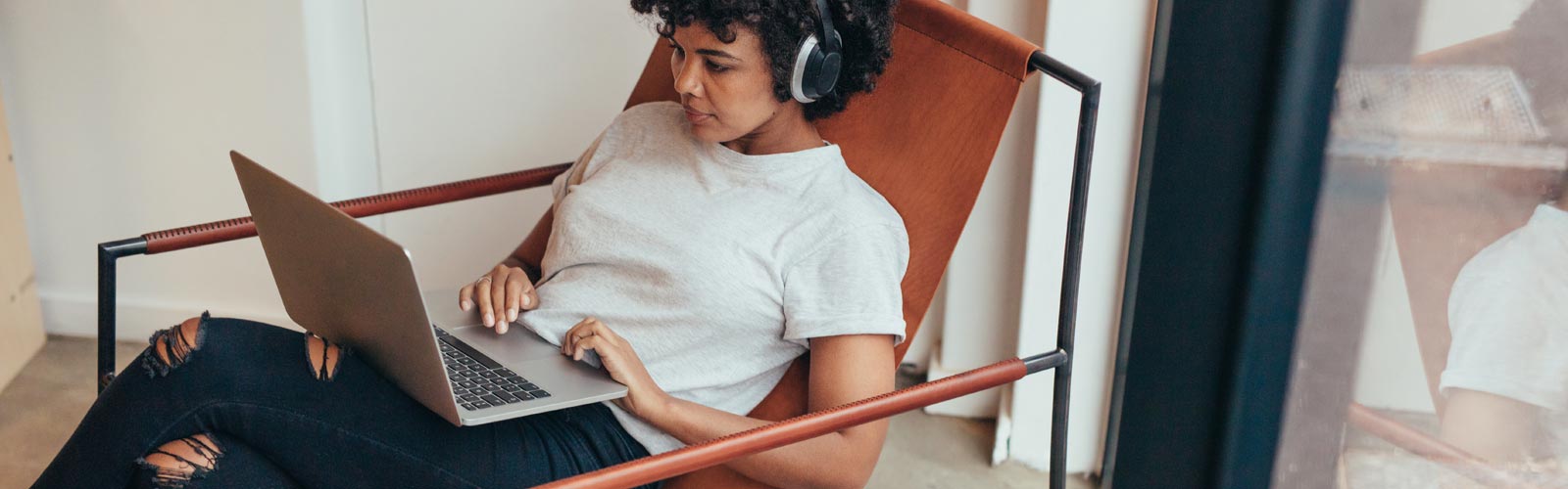 Woman with headphones on working on a laptop on a comfortable chair