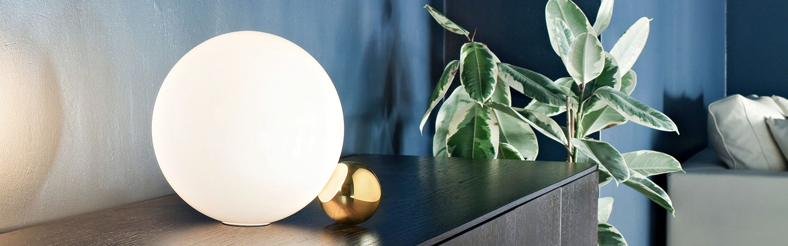 Bright white round lamp on a black cabinet next to a green indoor plant