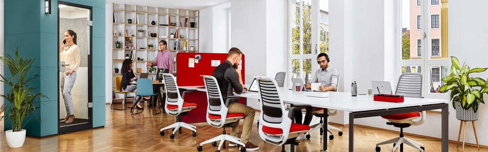 Steelcase blue meeting pod in the corner of a modern office populated with busy workers