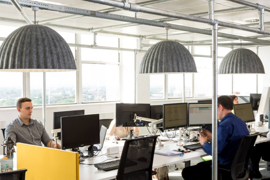 Large grey felt acoustic lampshades over an office bank desk with people working on laptops