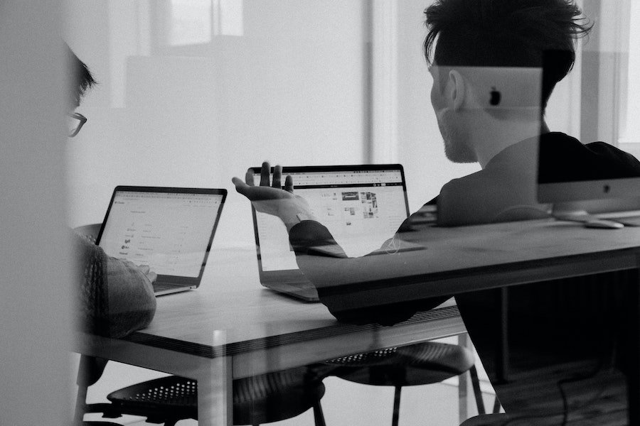Black and white image of two males in an office meeting room with open laptops