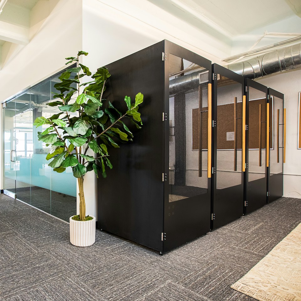 Black privacy booths in an office with grey carpet and green indoor plant