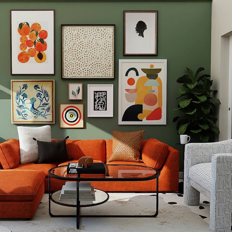 An orange sofa against a sage green wall with a collection of different size art print frames, on top of a white rug with a glass coffee table with black metal frame